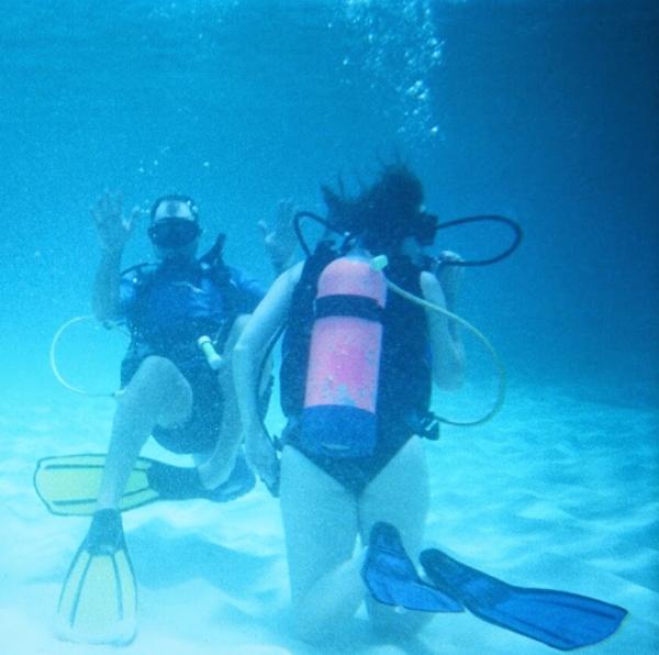 Two divers wave at the camera underwater in Anguilla